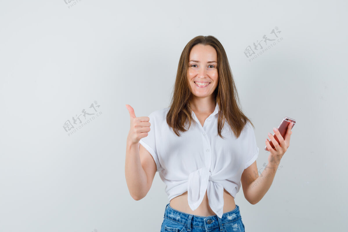 成人穿着白衬衫的年轻女士拿着电话 同时竖起大拇指 愉快地看着前面的景色服饰肖像电话