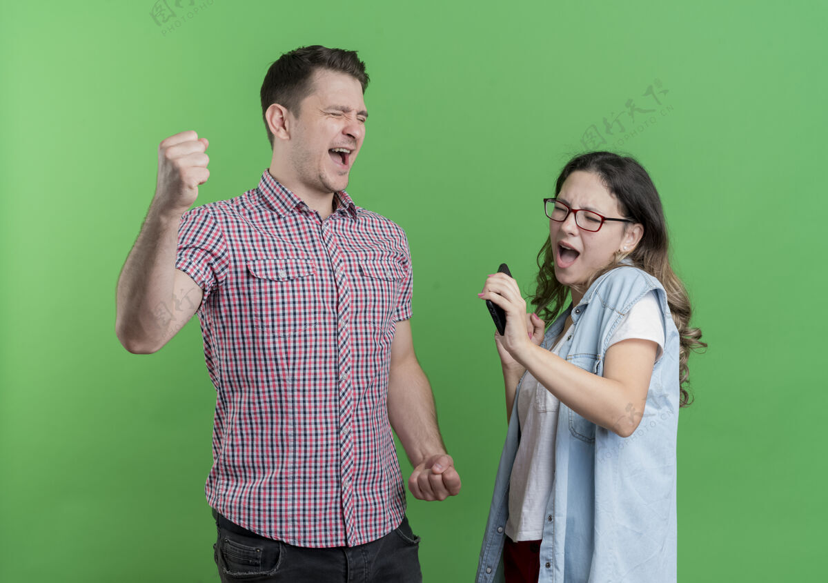 拳头一对穿着休闲服的年轻夫妇高兴而兴奋地握紧拳头站在绿色的墙上女人衣服兴奋