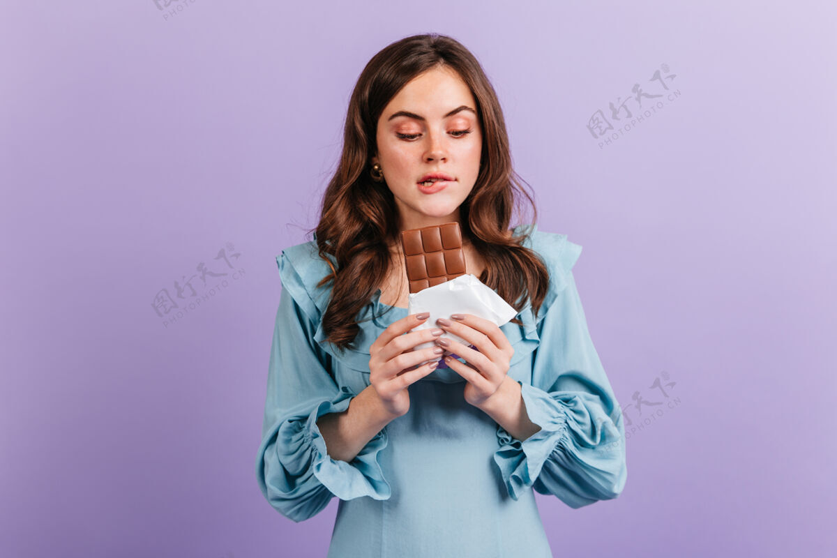 欢乐有趣的黑发女人咬着嘴唇期待美味的午餐的画像穿蓝色裙子的女孩看着美味的巧克力微笑人营养