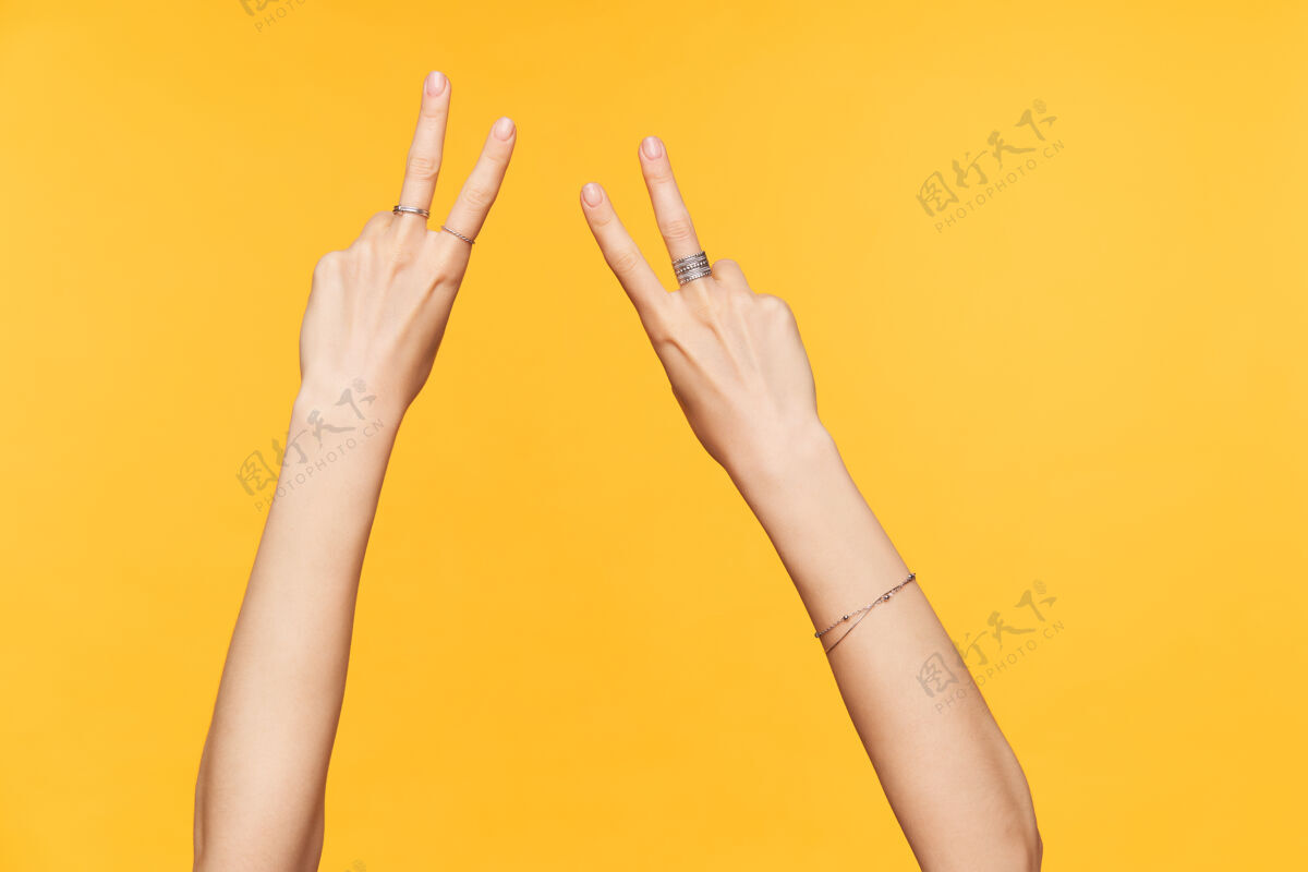特写摄影棚照片年轻的皮肤白皙的女性手与裸体美甲保持手指抬起 同时显示胜利的姿态 隔离在黄色背景下符号手臂语言