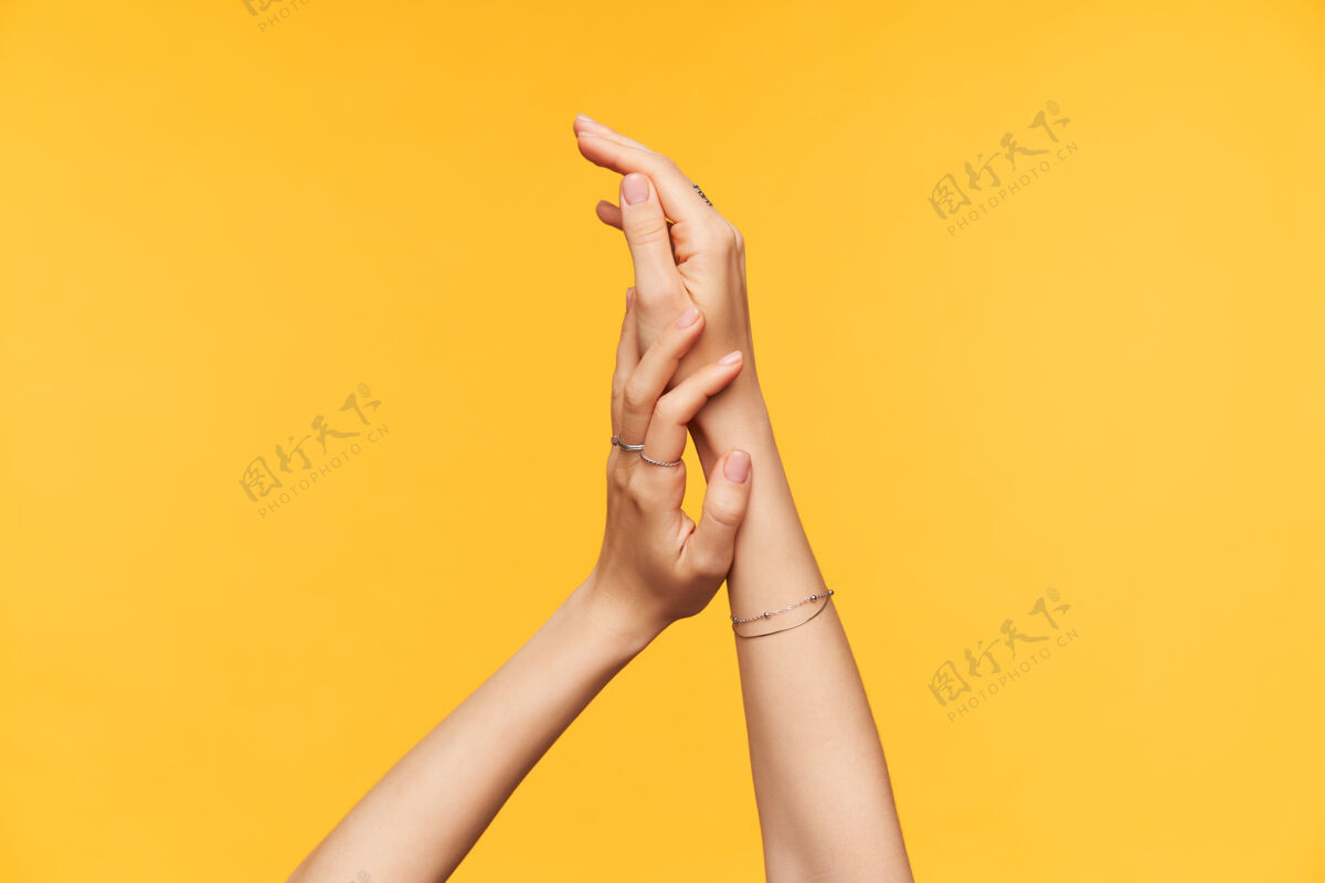 手臂室内拍摄的年轻女士皮肤白皙的手在涂面霜时轻轻地相互接触 隔离在黄色背景上身体和手护理概念成人手指女性