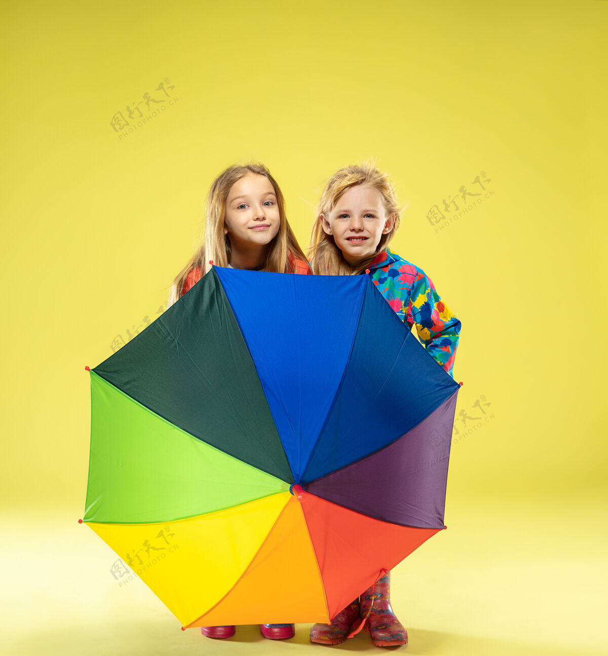 靴子黄色工作室墙上 一个穿着雨衣 手持彩虹色雨伞的时尚女孩的完整肖像休闲快乐欢呼