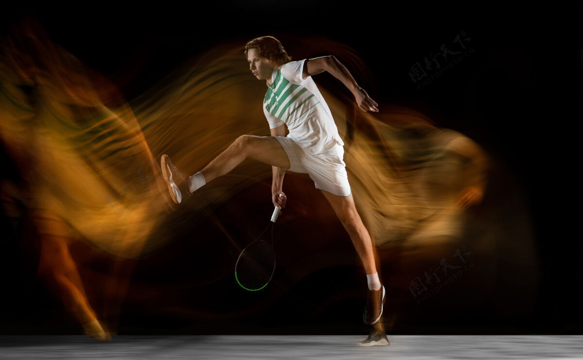 比赛年轻的白种人职业运动员在混合光的黑墙上打网球健身举行动作
