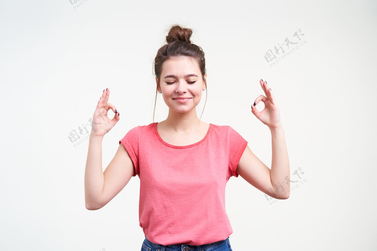 情绪一位面容讨人喜欢的棕色头发的年轻女士 双手紧闭 一边冥想 一边用mudra手势举手 站在白色背景上微笑表情T恤