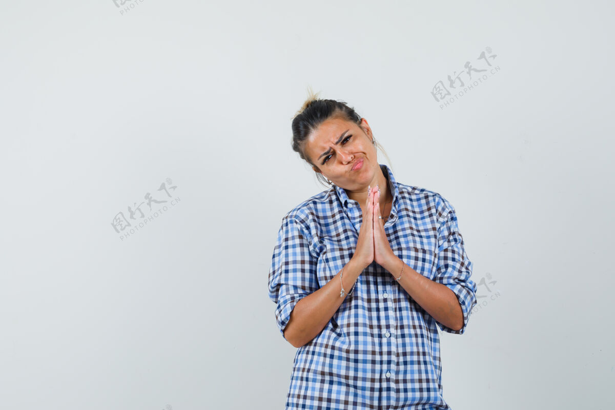 看起来一个穿着格子衬衫的年轻女子做着祈祷的手势 看上去很无助脸手势表演