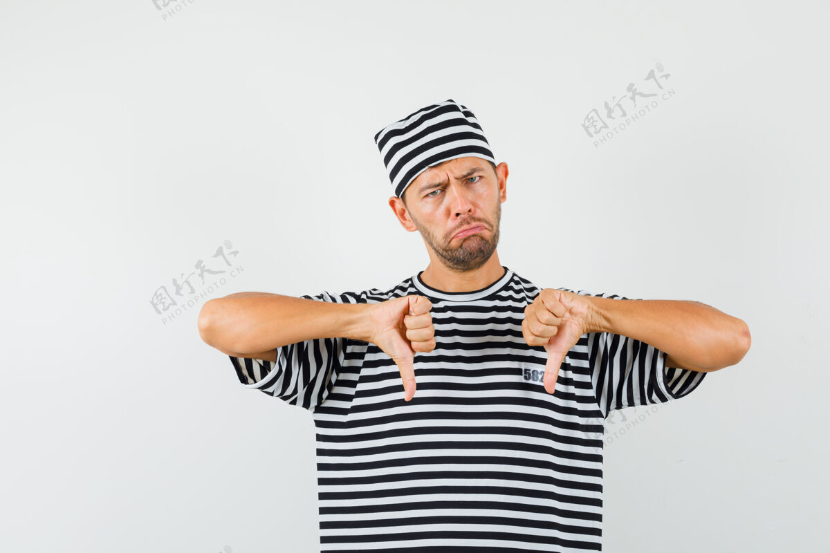 男人一个年轻人穿着条纹t恤 戴着帽子 大拇指朝下 看上去很失望看失望时尚