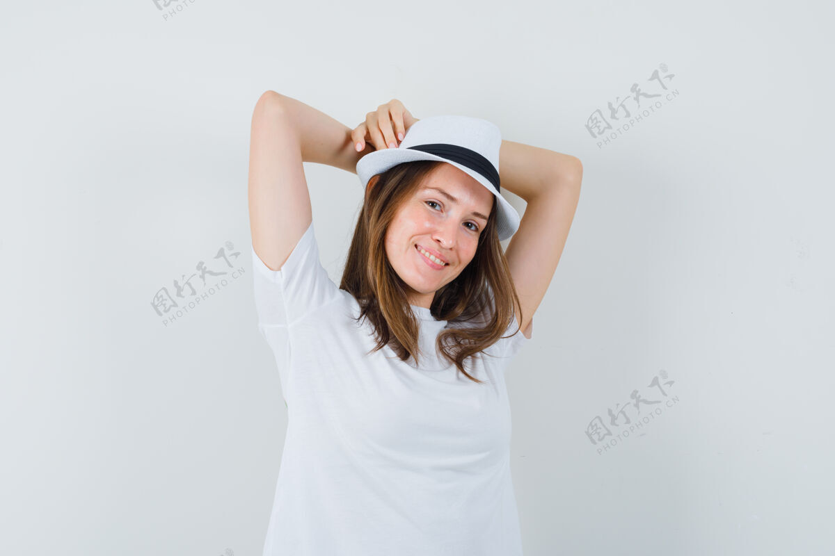放松年轻女子举着双手 头后穿着白色t恤 戴着帽子 看上去很放松期待脸提高
