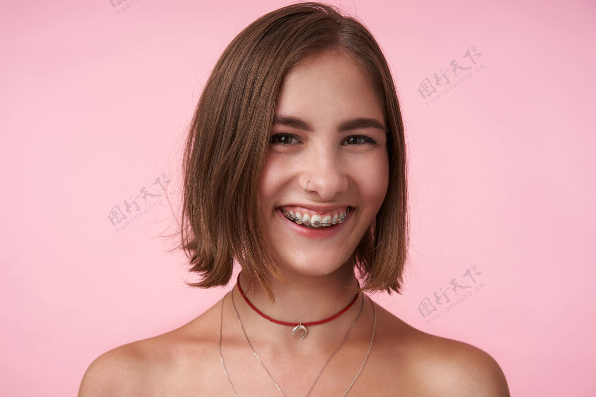 微笑年轻快乐的棕色眼睛 深褐色头发的女性 留着鲍勃式的发型 微笑着快乐地看着前面 隔着粉红色的墙姿势欧式发型
