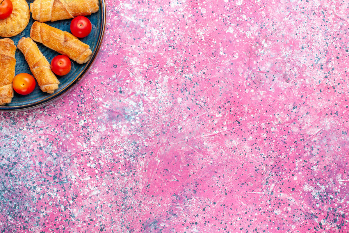 生的顶视图甜美美味的百吉饼烤糕点托盘内与李子在粉红色的表面蛋糕饼干饼干