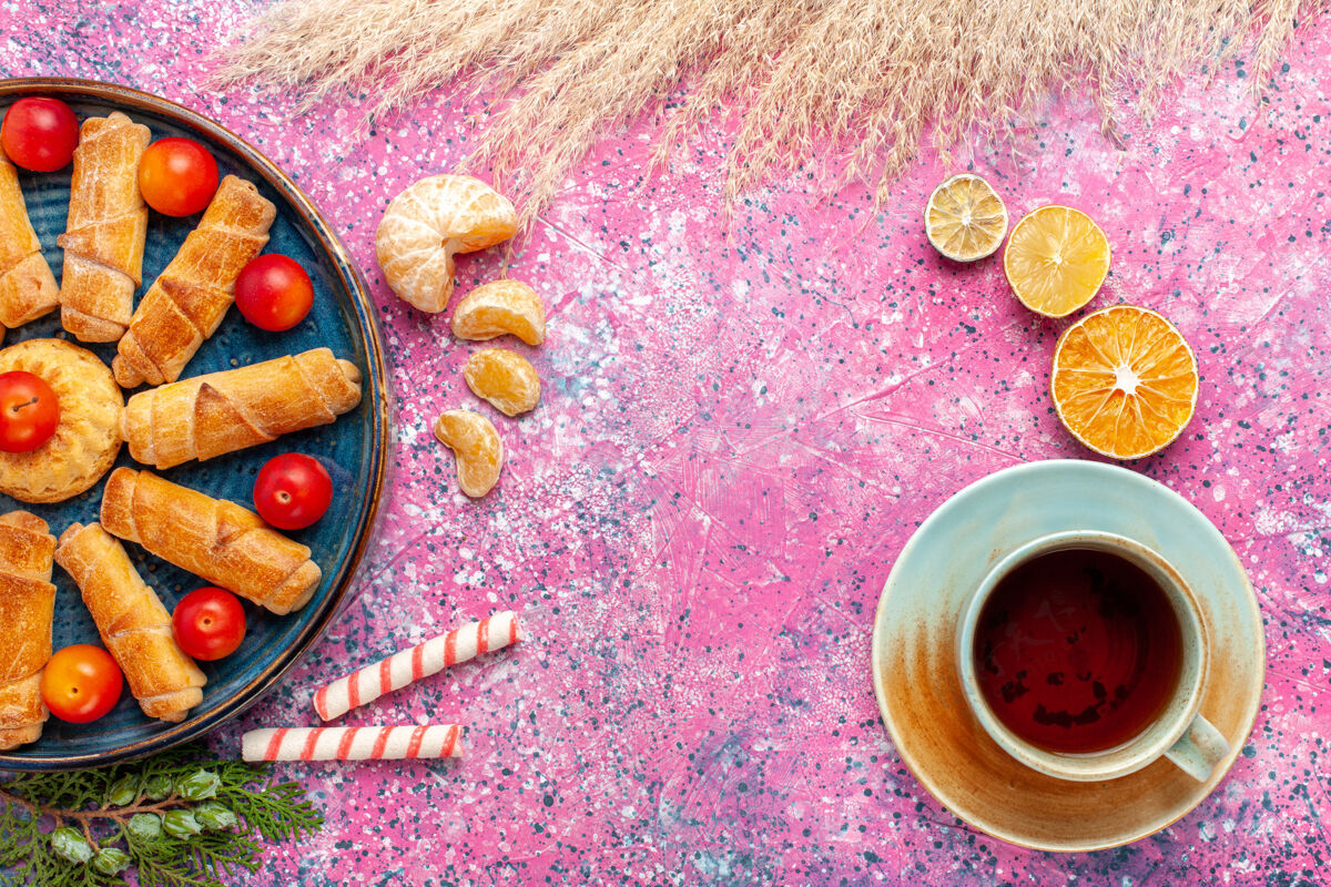 美味顶视图甜甜可口的百吉饼在托盘内与酸李子和茶在淡粉色的桌子上糖百吉饼茶