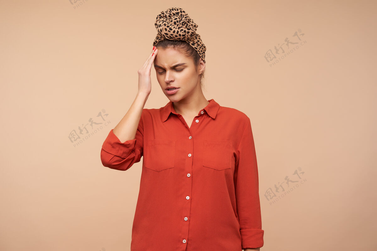 模特不幸的年轻黑发女子戴着头巾 打着结 站在米色的墙上 穿着红衬衫 眼睛紧闭 手举到头上触摸美女爱情
