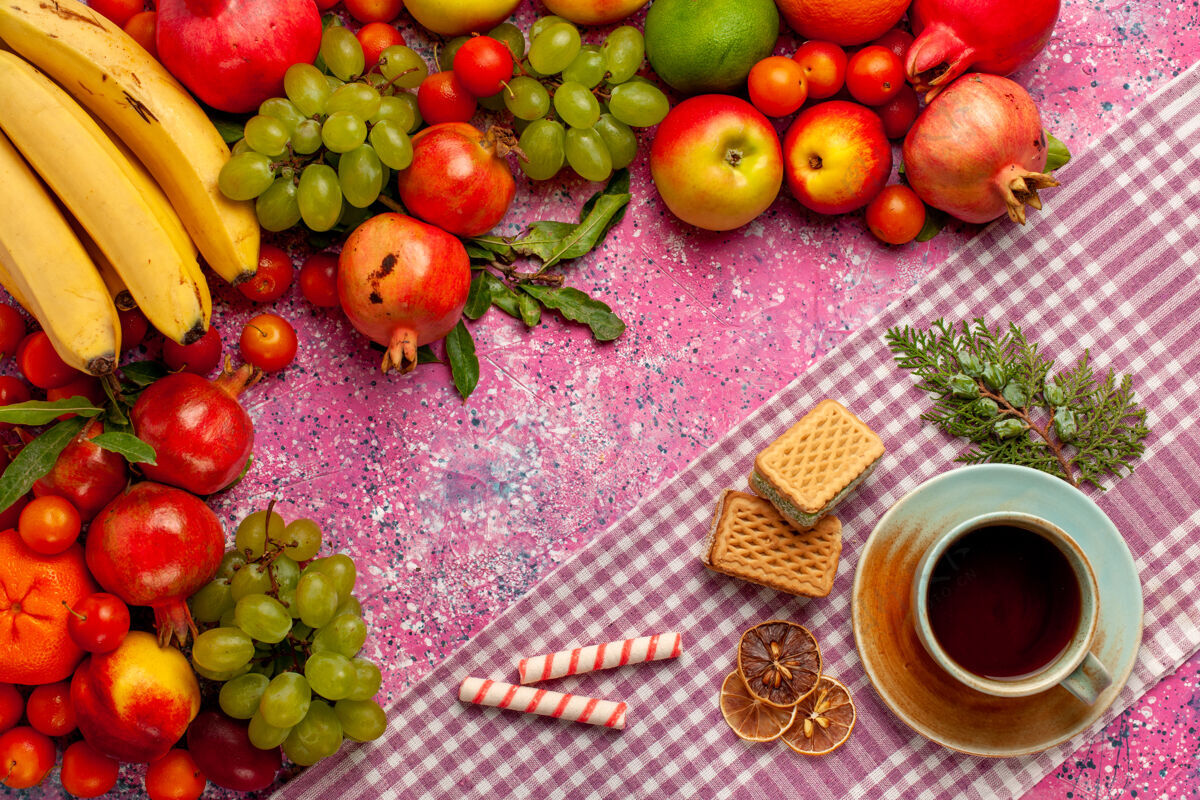 多汁的顶视图新鲜水果组成五颜六色的水果与一杯茶和华夫饼在粉红色的表面苹果茶水果