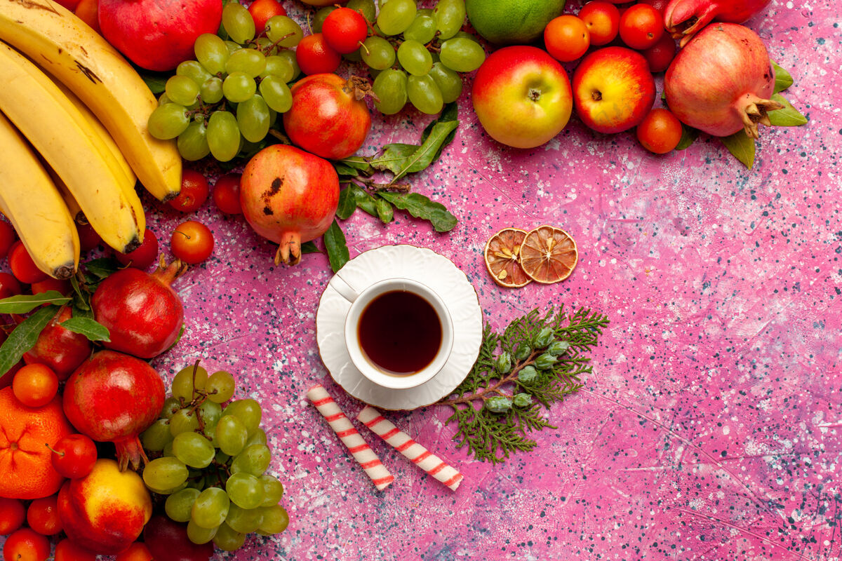 树顶视图新鲜水果组成五颜六色的水果与一杯茶在粉红色的表面苹果可食用的水果葡萄