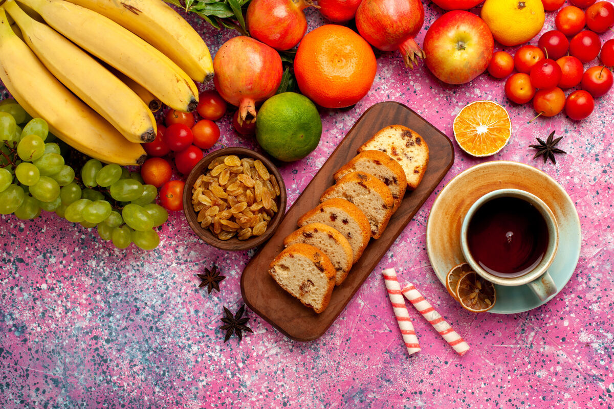 维生素俯瞰美味的水果组成与切片蛋糕和一杯茶在粉红色的桌子上异国情调美味茶