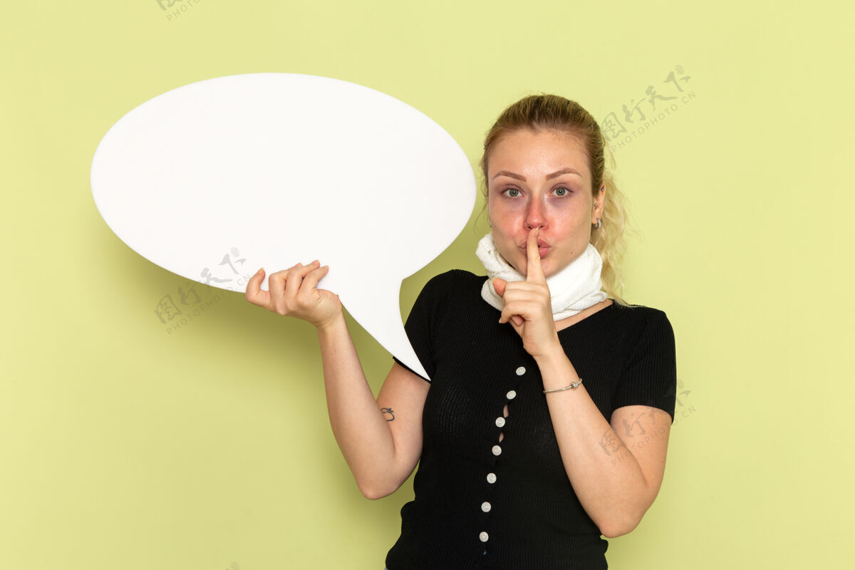 生病的正面图年轻女子手握巨大的白色标牌 在绿墙上要求安静生病吃药生病感觉的冰棍生病的