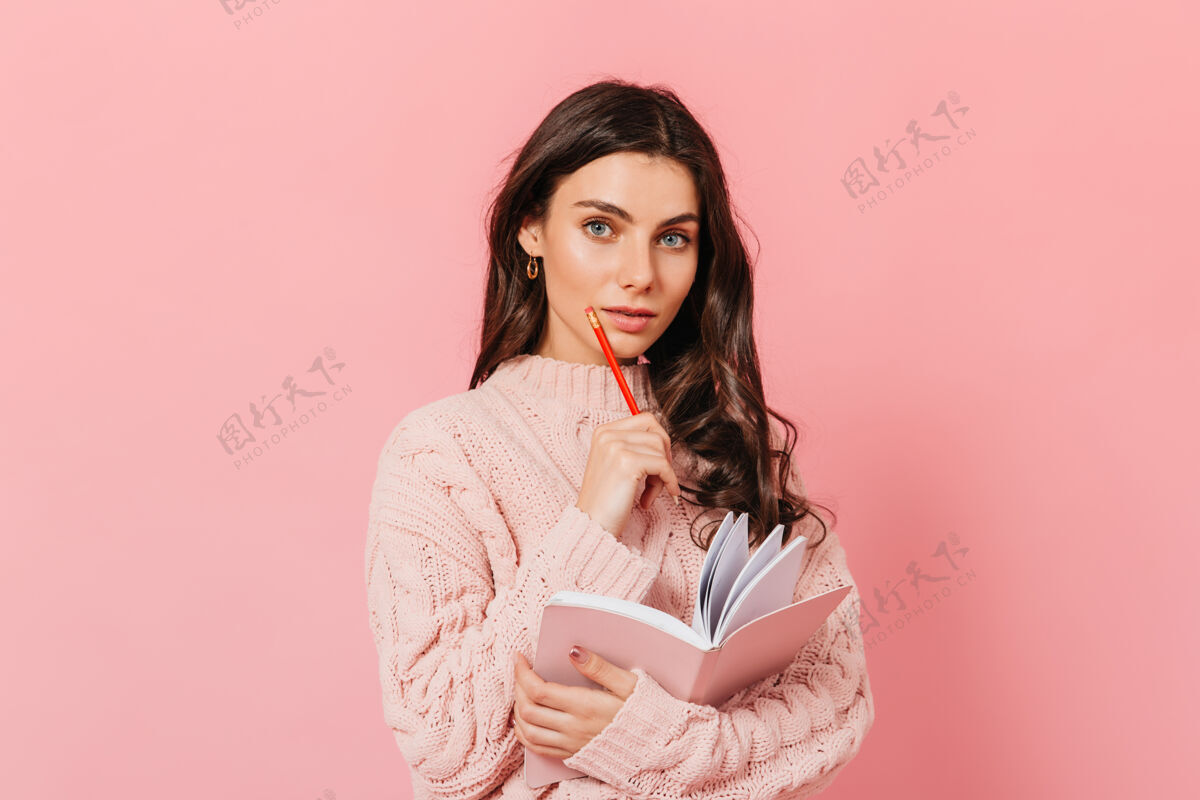发型可爱的蓝眼睛女孩在粉色背景上若有所思地摆姿势卷发女士拿着红铅笔和日记蓝眼睛正面学生