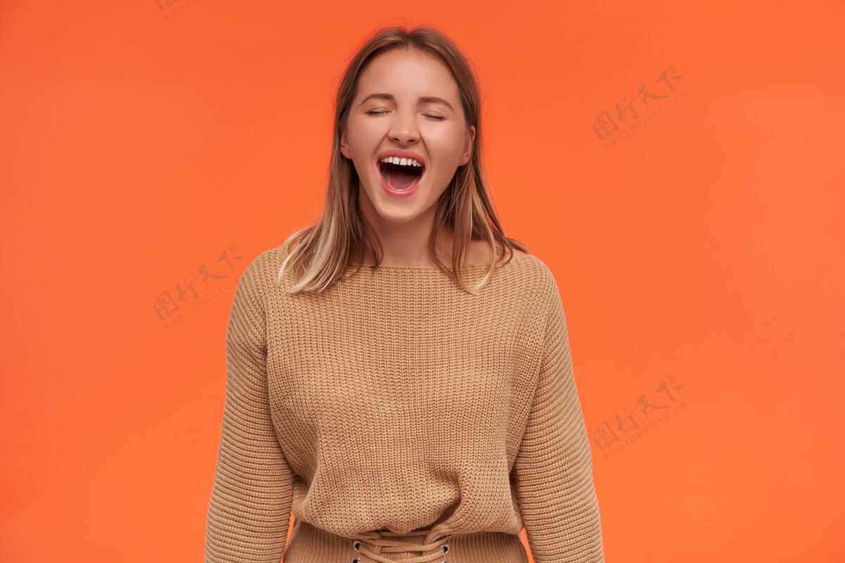 表情漂亮的年轻开朗的金发短发女士 自然的妆容 闭上眼睛 快乐地笑着 隔着橘色的墙表达欧式女衬衫