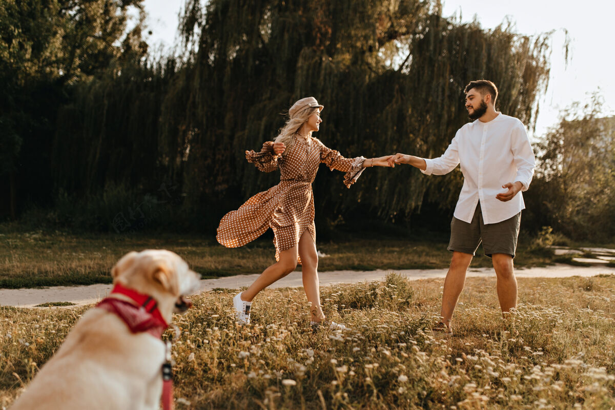 拉布拉多一个女人穿着棕色的衣服 戴着棕色的帽子 一个男人穿着短裤和衬衫 在公园里闲逛 带着狗散步散步动物狗