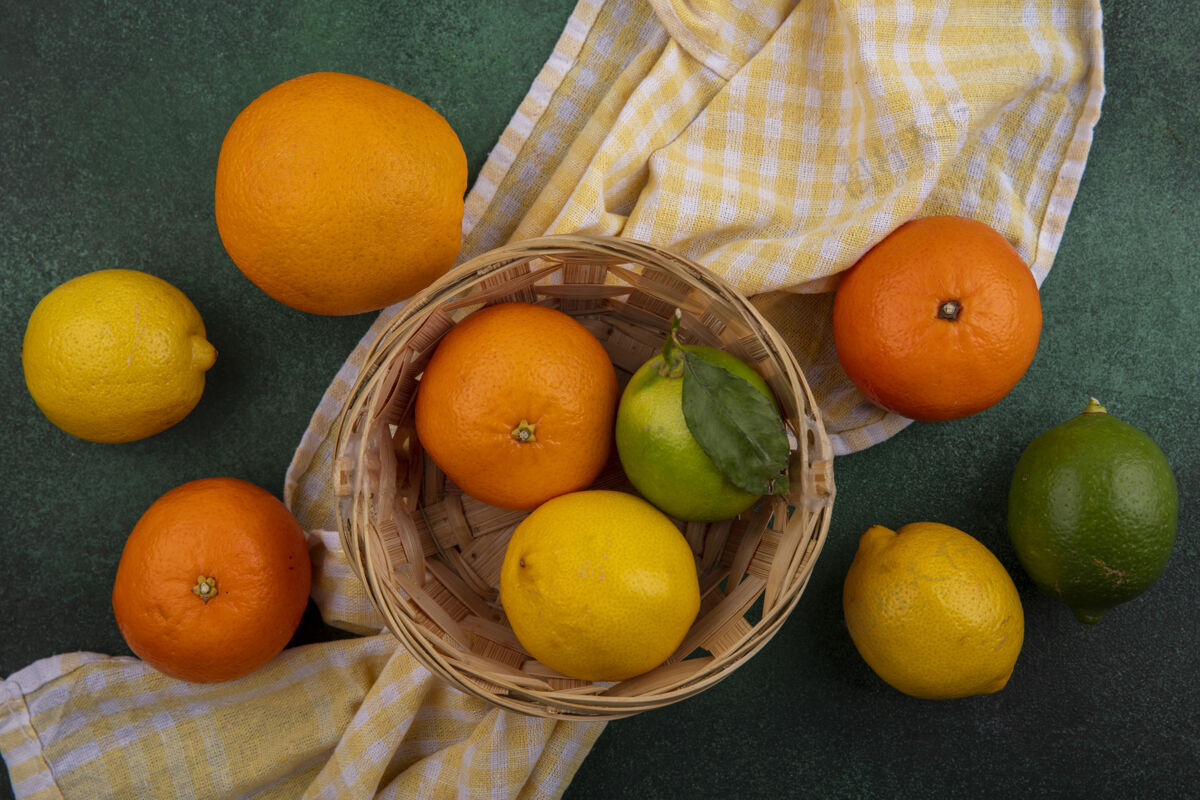 上衣顶视图橙色柠檬和酸橙在一个篮子里黄色格子毛巾在绿色的背景下毛巾景观青柠色