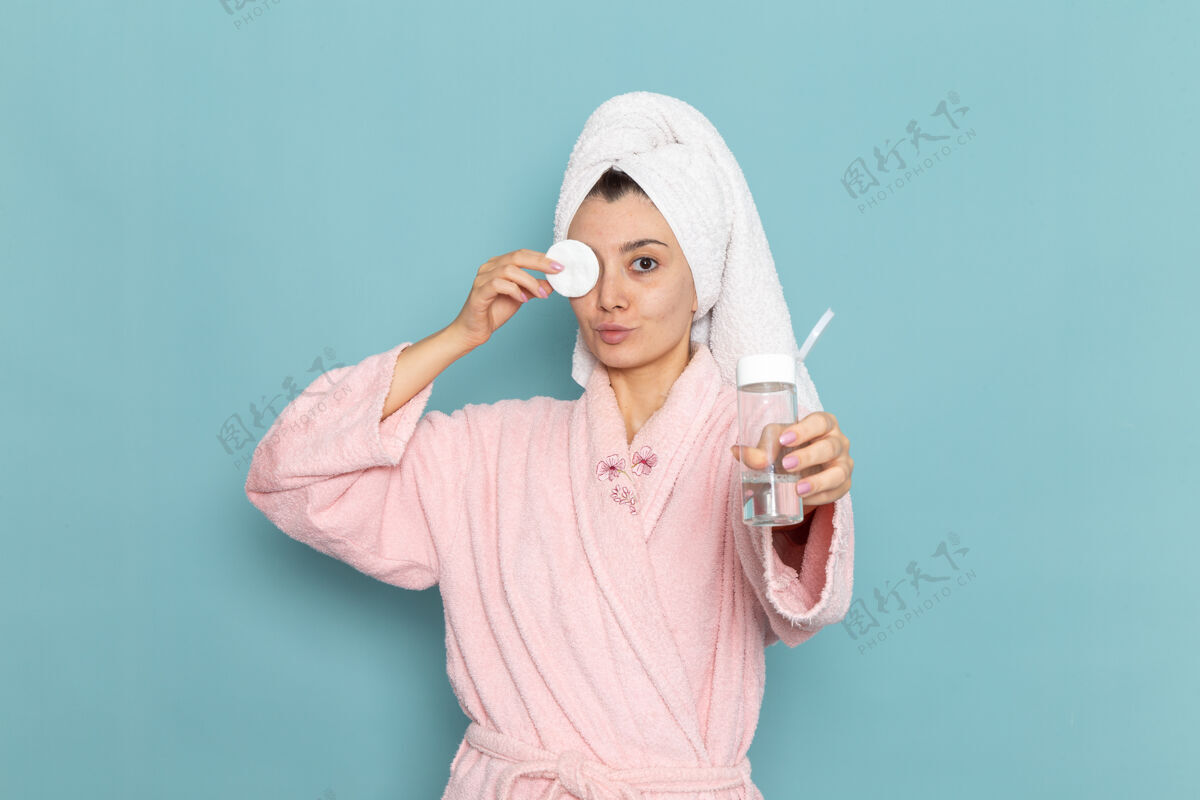 年轻人正面图身着粉色浴袍的年轻女性在蓝色墙壁上洗脸化妆淋浴清洁美容自护霜浴袍清洁奶油
