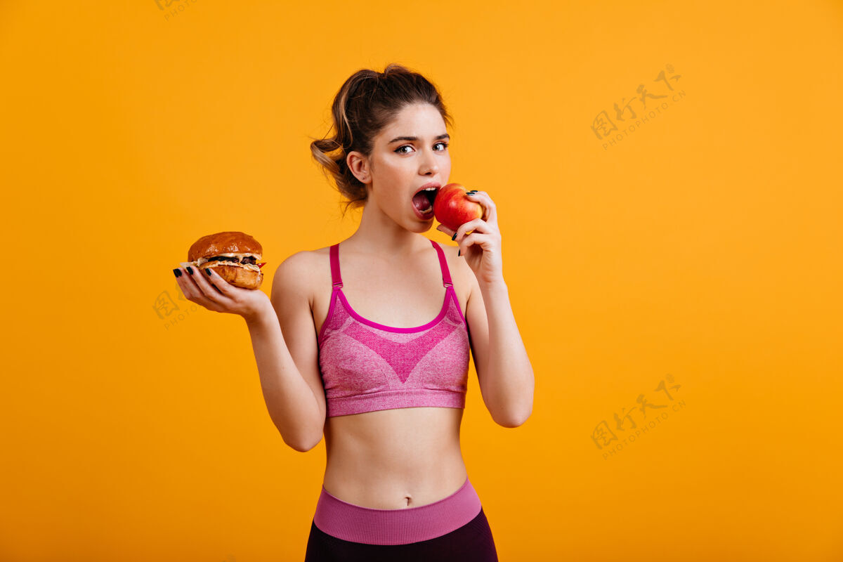 芝士汉堡运动的女人在橘色的墙上吃红苹果食物减肥女模特