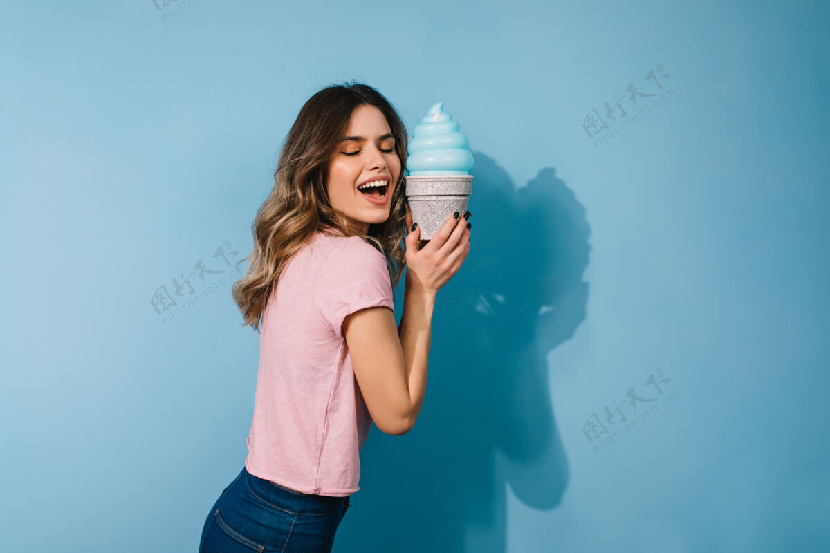 模型摄影棚拍摄的兴奋的女人和冰淇淋隔离在蓝色墙上欢笑卷曲食物