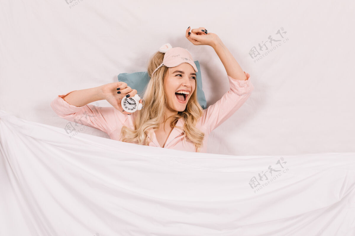 早起戴着睡眠面罩躺在床上的笑女人金发小睡成人