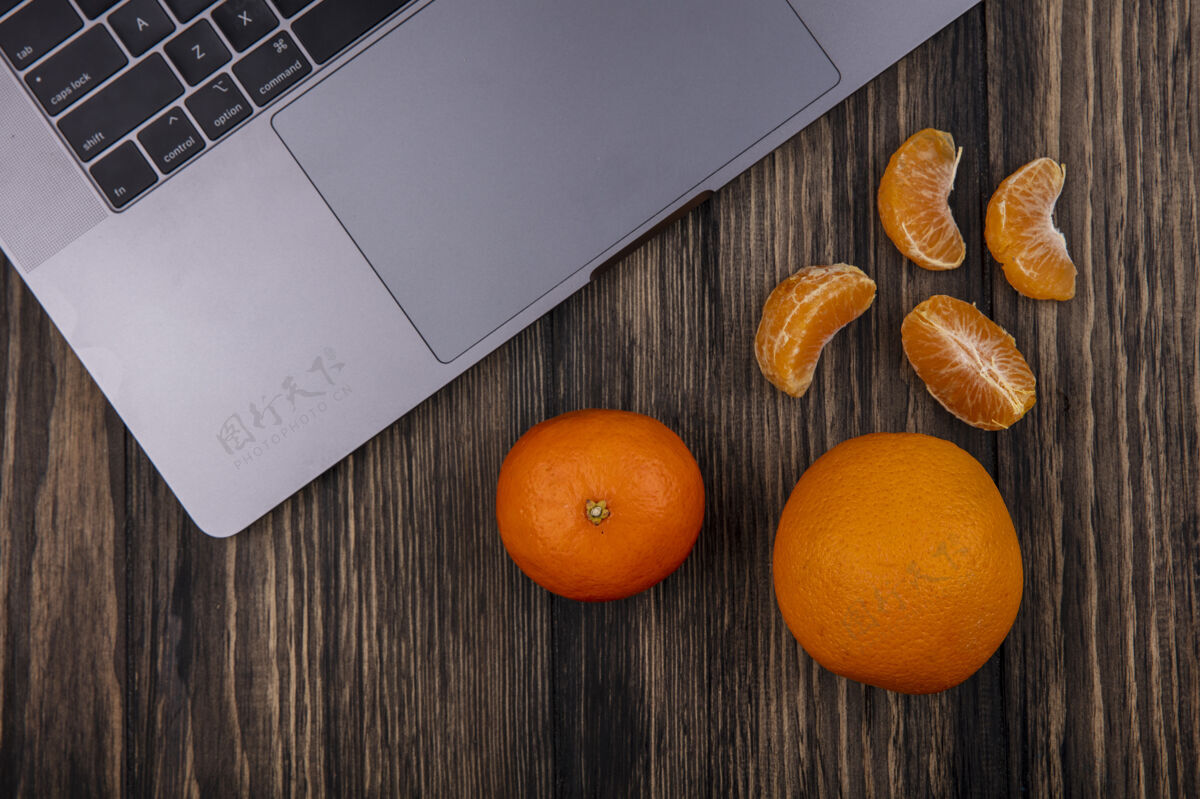 顶部顶视图与削皮楔和木制背景上的笔记本电脑桔子木材橘子水果