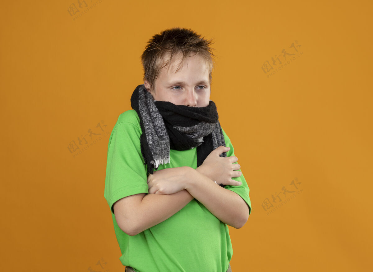 橘子生病的小男孩穿着绿色t恤 脖子和嘴上围着暖和的围巾 站在橘色的墙上感觉不舒服 发烧感冒疾病周围感觉