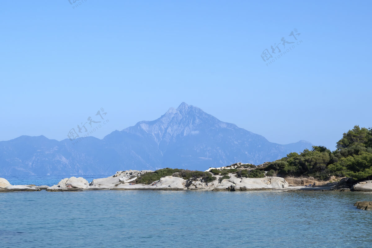 岩石爱琴海沿岸有岩石和休息的人 远处有山 前景是绿意盎然 蓝色的海水 希腊岩石镁砂海景