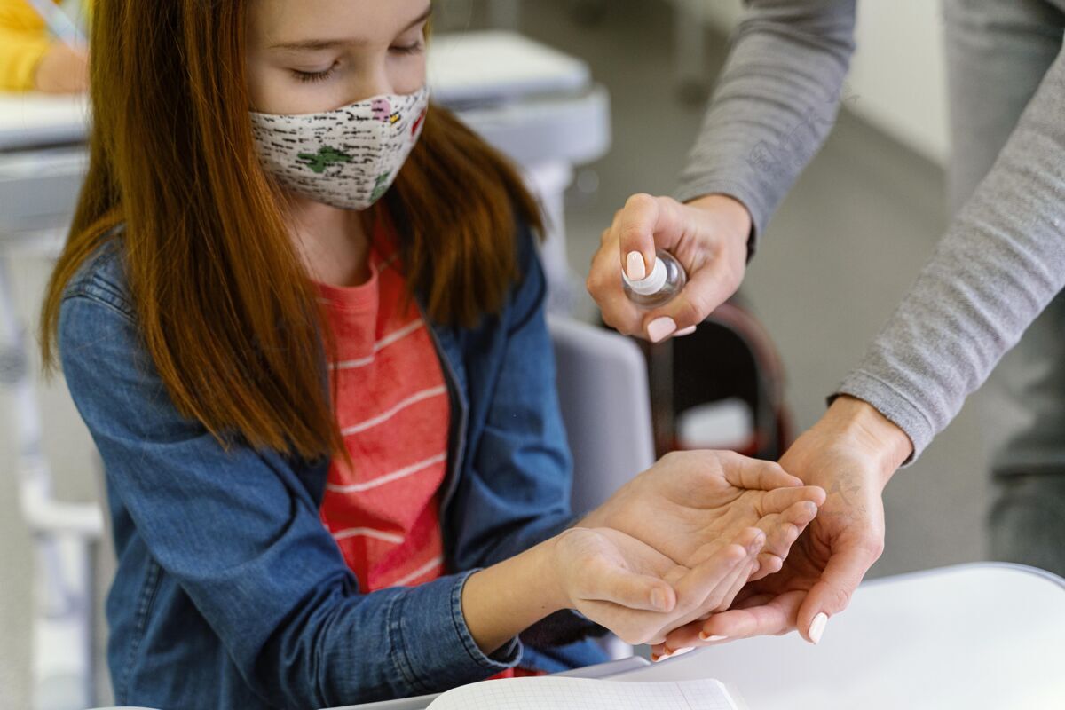 洗手液戴着医用口罩的小女孩从老师那里得到洗手液冠状病毒家教教育