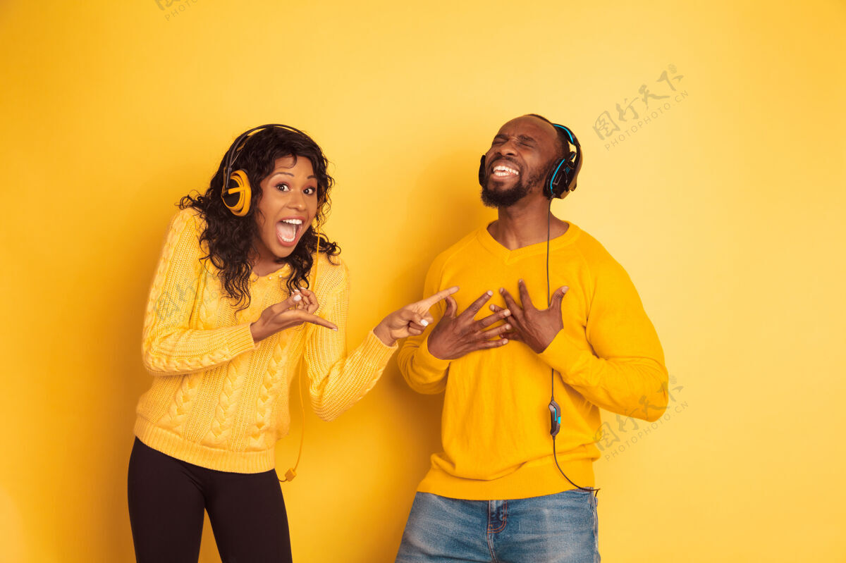 看年轻感性的非裔美国人 穿着黄色背景的明亮休闲服美丽的情侣人类情感的概念 面部表情 关系她指的是唱歌的男人明亮化妆品笑