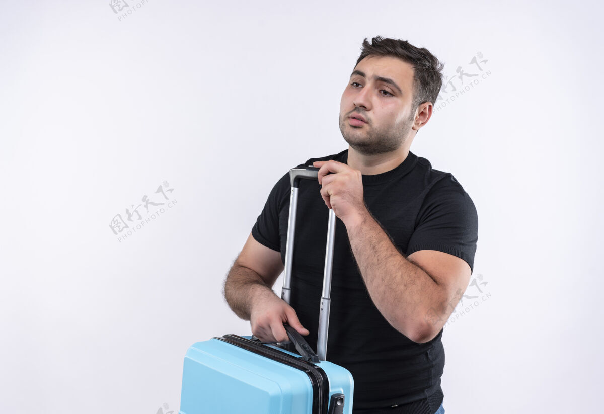 站着站在白墙上 一个穿着黑色t恤的年轻旅行家拿着手提箱 脸上带着悲伤的表情望向一边市民脸悲伤