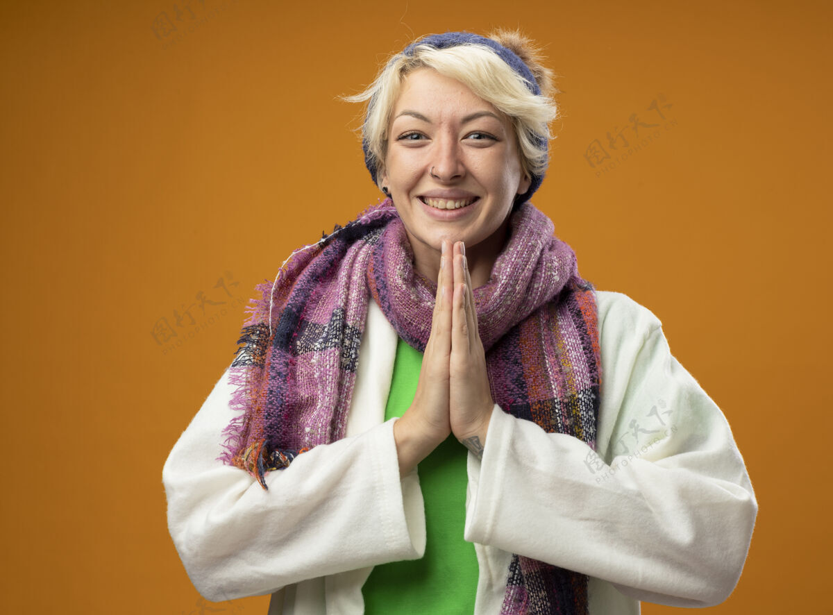 女人生病的不健康的女人 短发 戴着暖和的围巾 戴着帽子 手拉手 站在橘色的墙上祈祷 感觉好多了一起喜欢不健康