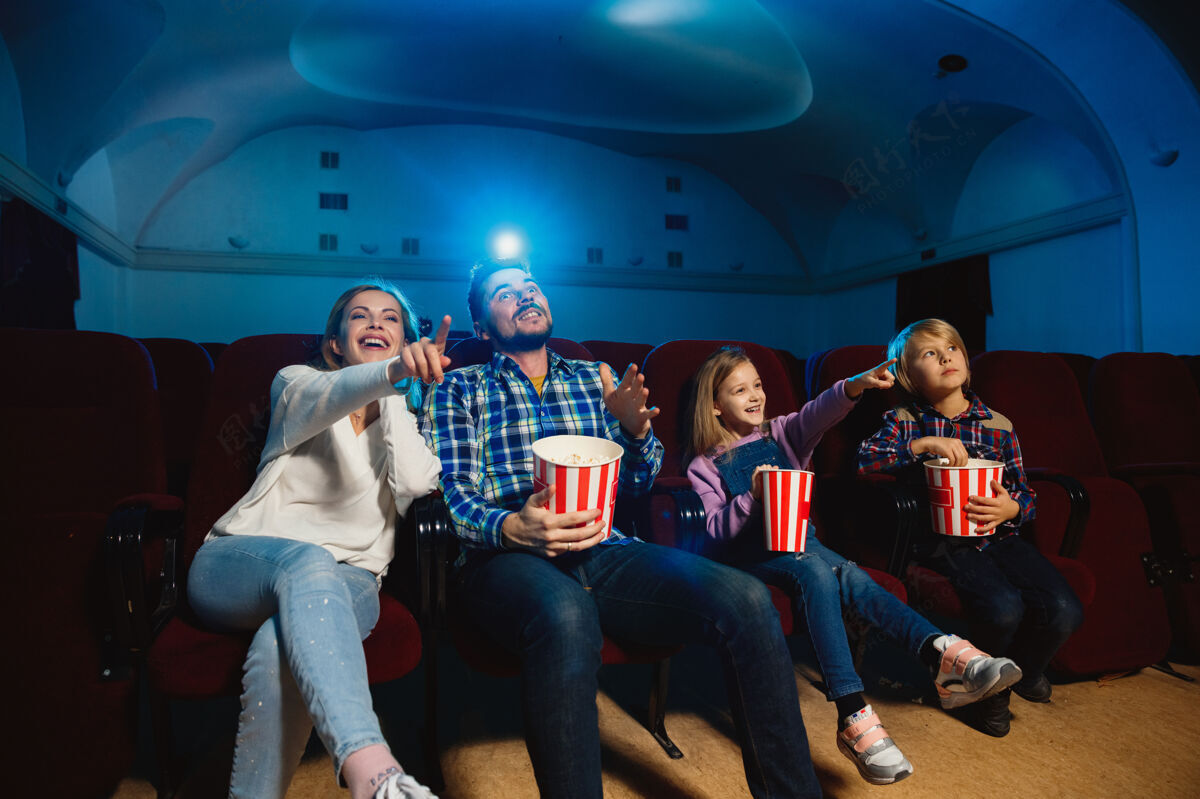 电影年轻的白种人家庭在电影院 房子或电影院看电影看起来富有表现力 惊讶和情绪化独自坐着玩关系 爱情 家庭 童年 周末时间看约会电影院