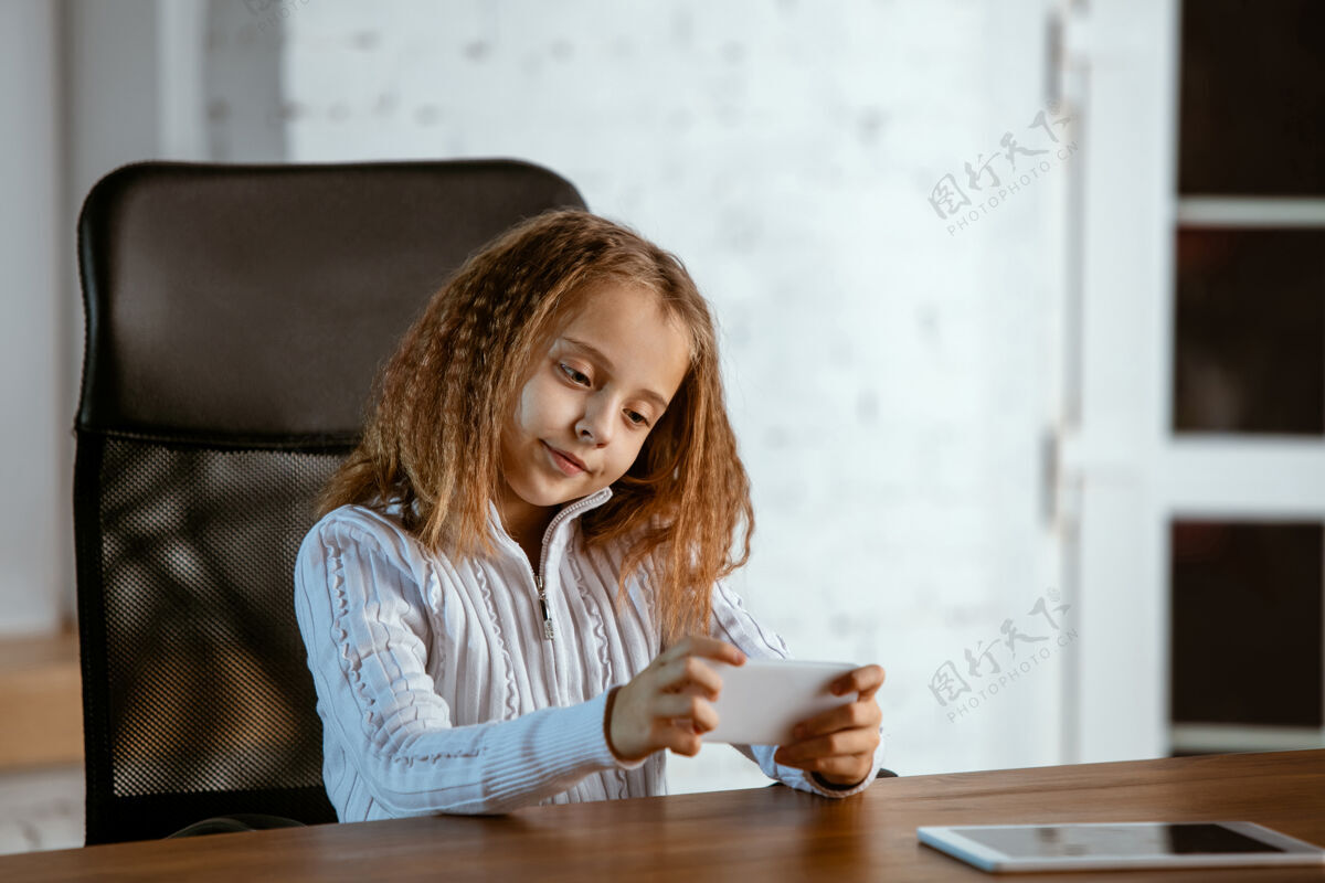 桌子年轻的白人女孩的肖像看起来梦幻 可爱和快乐抬头看 坐在室内的木桌与平板电脑和智能手机未来的概念 目标 梦想购买 可视化梦想房子爱