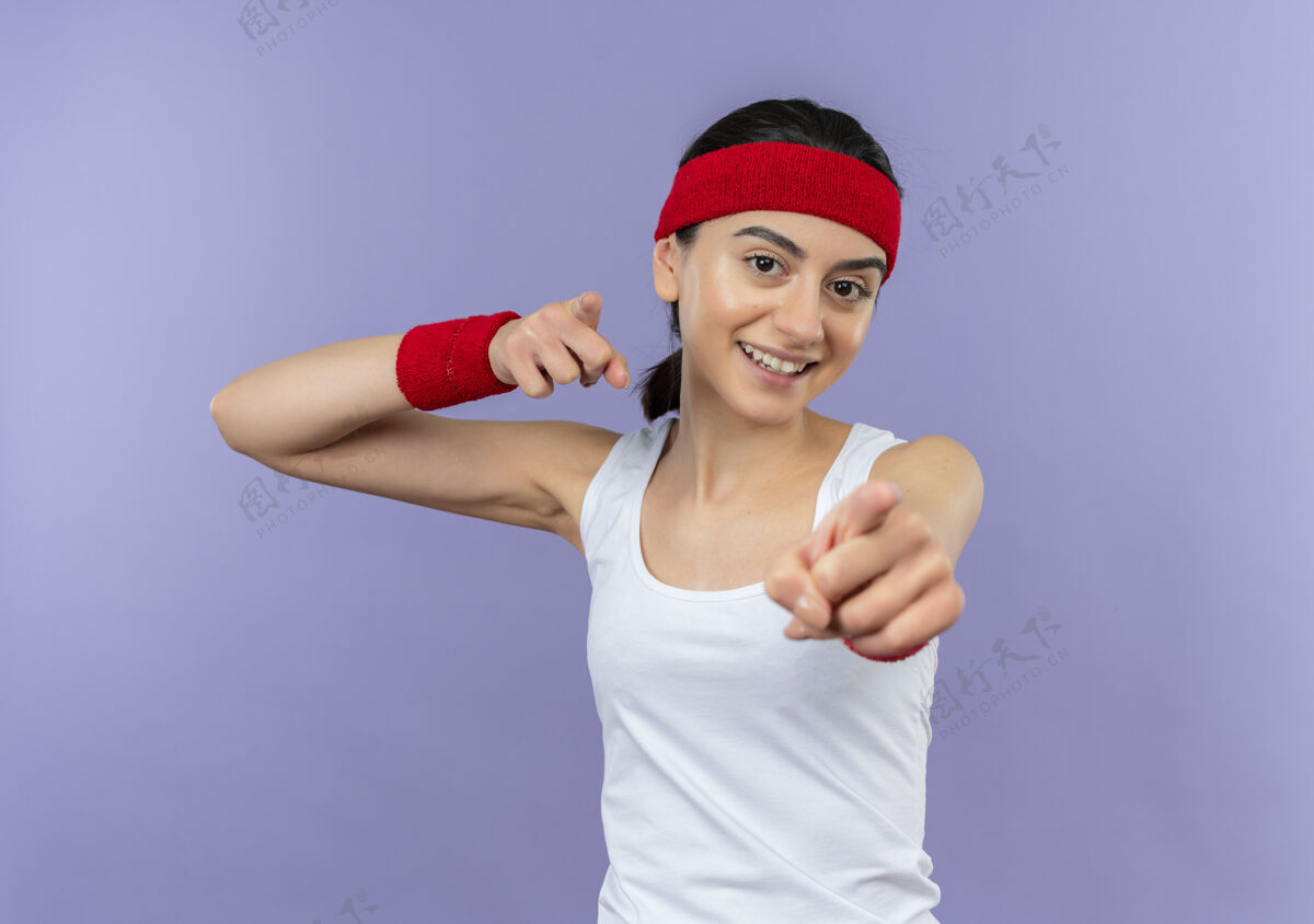 人身穿运动服的年轻健身女 戴着头巾 食指指着镜头 站在紫色的墙上 脸上洋溢着欢快的笑容市民微笑目录