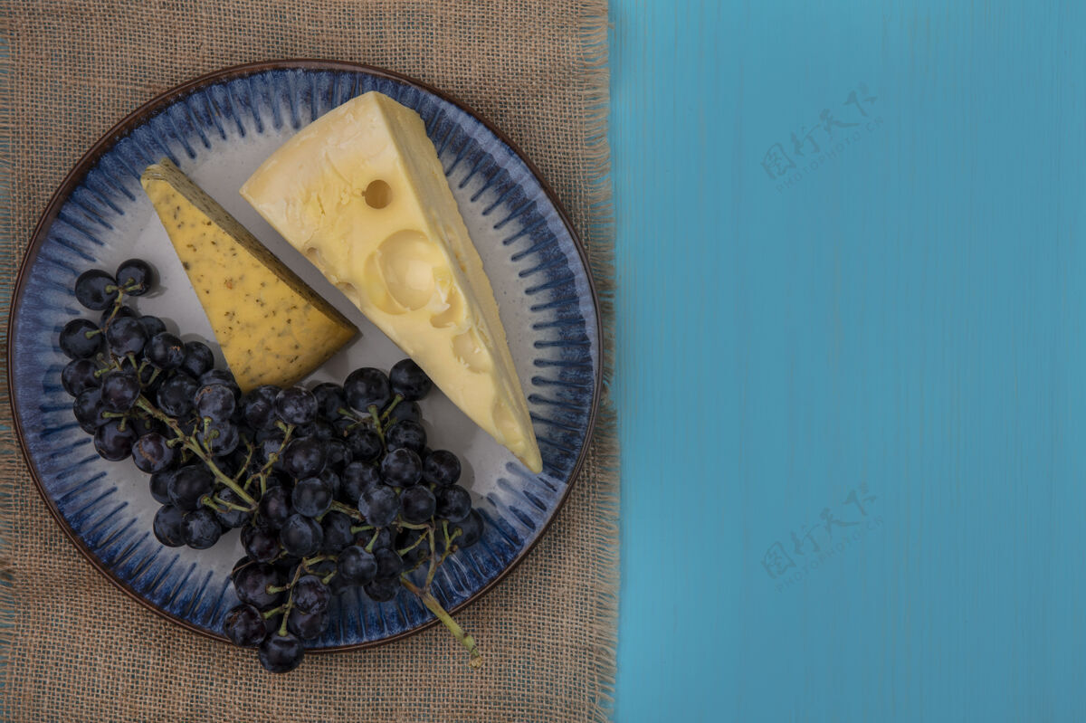 绿松石色顶视图复制空间黑色葡萄与奶酪片在一个盘子上米色餐巾在一个绿松石背景顶部视野空间