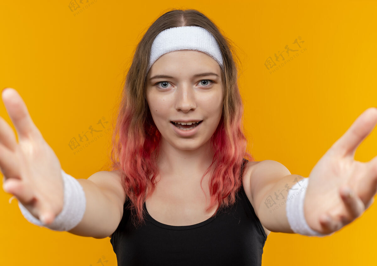 运动身着运动服的年轻健身女士站在橙色的墙上做欢迎手势欢迎运动手