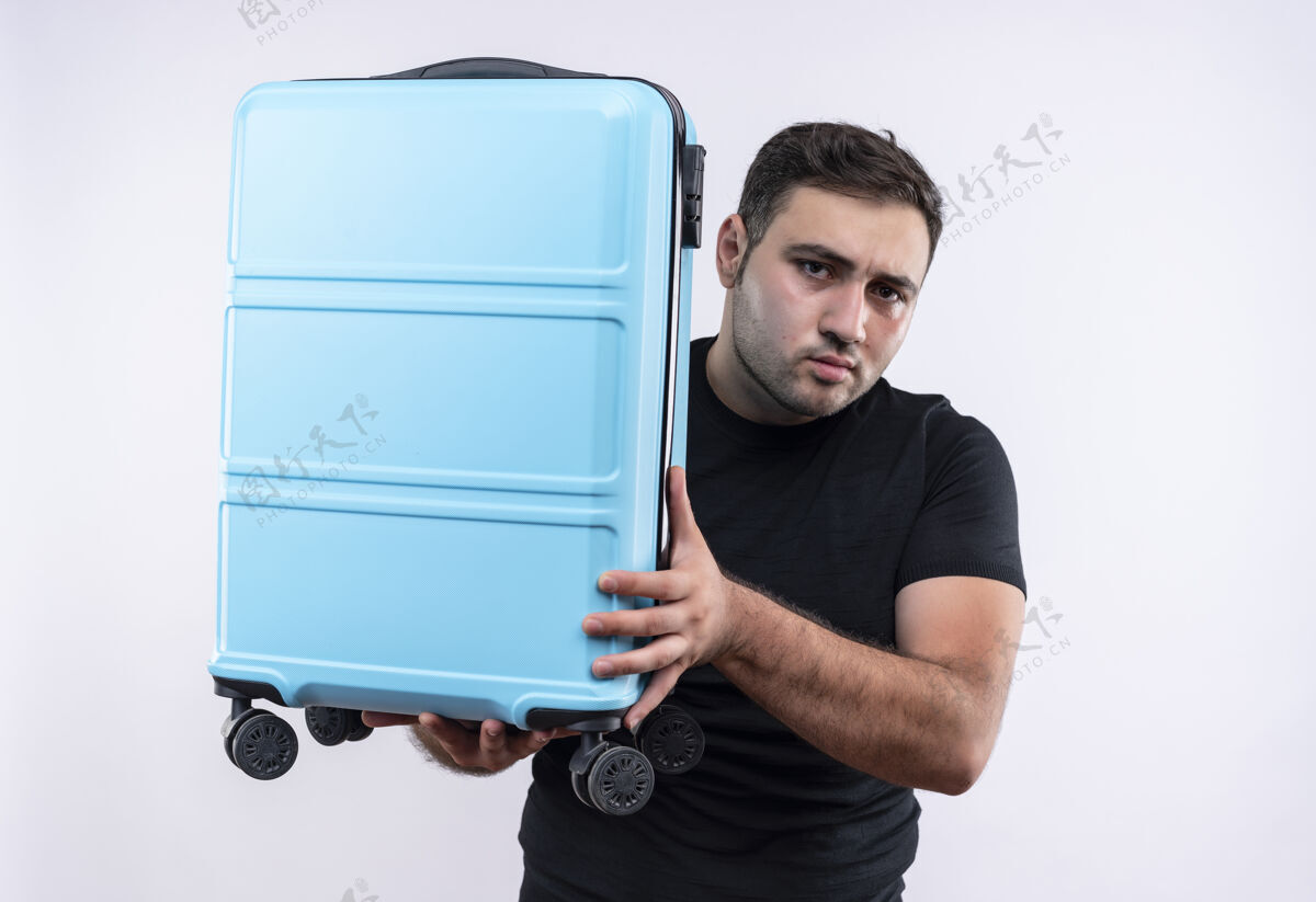 夏天穿着黑色t恤的年轻旅行家拿着手提箱站在白色的墙上假期人看