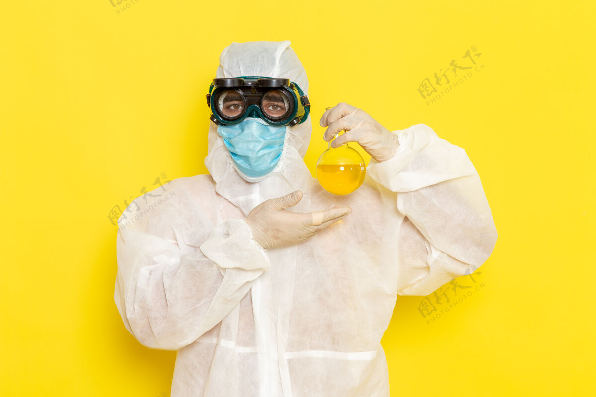 化学正面图穿着特殊防护服的男科学工作者拿着黄色表面上有黄色溶液的烧瓶危险工人保护
