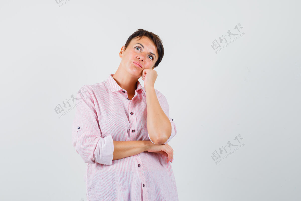 瘦穿着粉色衬衫的女性斜靠在举起的拳头上的脸颊 看起来沉思前视图年轻疾病肖像