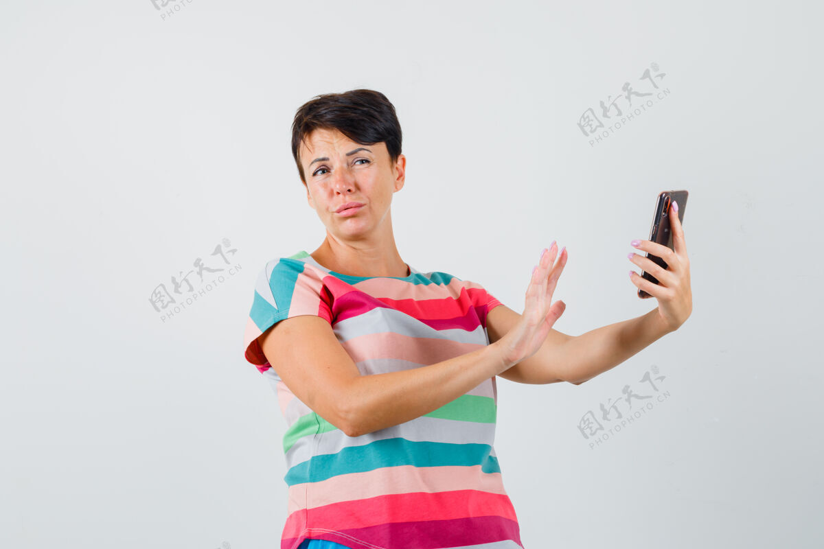 面罩穿着条纹t恤的女性一边用手机 一边显示拒绝手势 前视图电话条纹手机