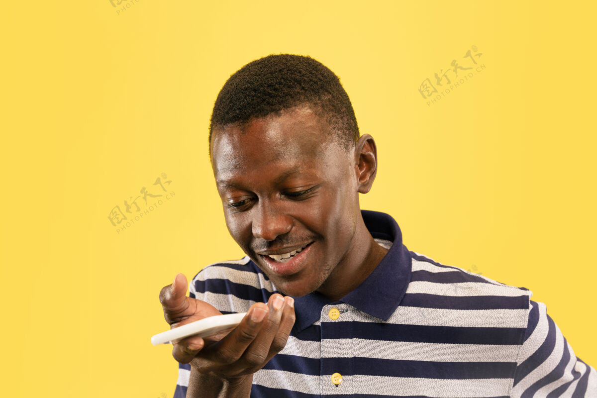 幸运年轻的非洲裔美国男子用智能手机隔离在黄色的工作室背景下 面部表情美丽的男性半身肖像人类情感的概念 面部表情男性移动微笑