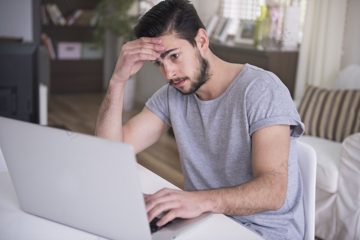 悲伤疲倦的年轻人在家里用他的笔记本电脑工作时尚无线互联网问题