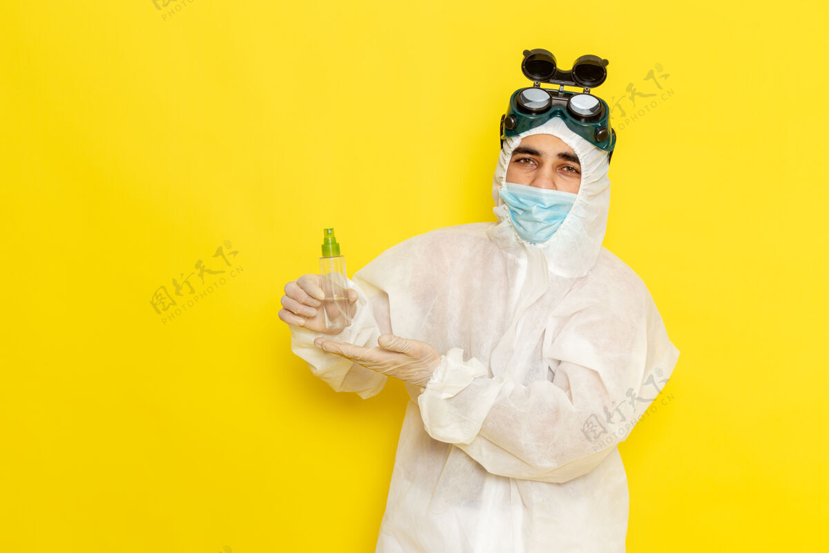 烧瓶正面图穿着特殊防护服的男科学工作者拿着黄色表面上的喷雾瓶面具科学特殊
