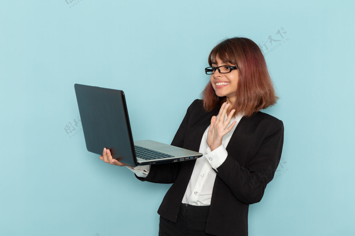 女前视图穿着西装的女办公室工作人员拿着笔记本电脑在蓝色的表面上使用它工作工作笔记本电脑