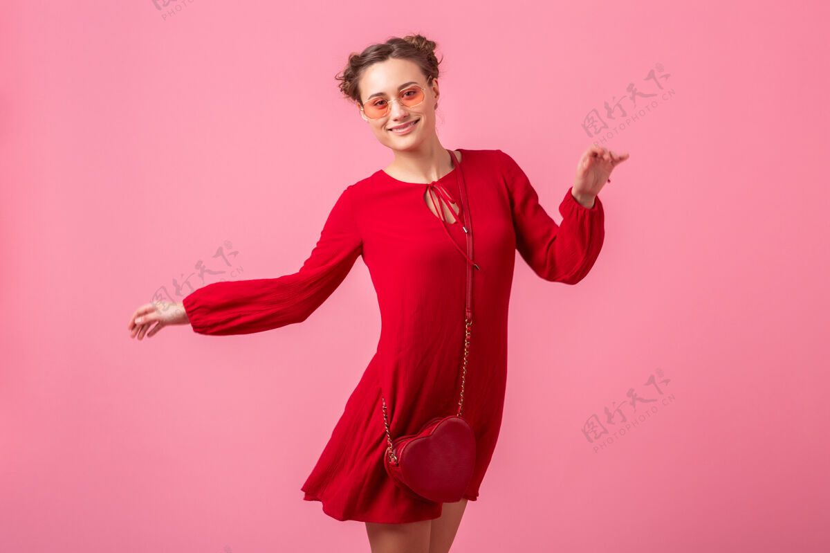 女孩迷人的快乐微笑的时尚女人穿着红色的时髦连衣裙在粉色的墙壁上跳跃奔跑孤立 春夏的时尚潮流 圣瓦伦尼特节 浪漫的心情调情的女孩钱包身高充分