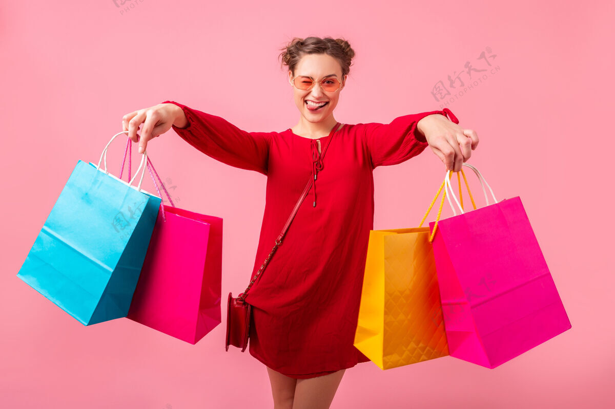 女孩迷人快乐搞笑情感时尚女性购物狂身着红色新潮连衣裙手捧五颜六色购物袋在粉色墙壁上孤零零出售 销售兴奋 春夏时尚潮流现代太阳镜购买