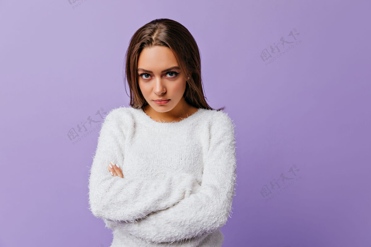 成人长发黑发 绿眼睛 被冒犯了 站在封闭的姿势在淡紫色上穿着白色温暖毛衣的年轻女孩的特写肖像室内肖像魅力